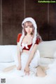 A woman in a santa outfit sitting on a bed.