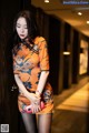 A woman in an orange dress leaning against a wall.