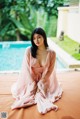 A woman in a pink robe sitting by a pool.