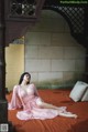 A woman in a pink dress sitting on a bed.