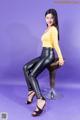 A woman in a yellow top and black leather pants sitting on a stool.