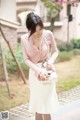 A woman in a pink shirt and white skirt holding a white purse.