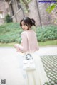 A woman in a pink top and white skirt holding a white bag.