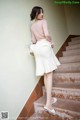 A woman in a pink shirt and white skirt is standing on some stairs.