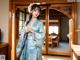 A woman in a blue kimono standing in front of a door.