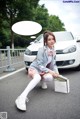 A woman sitting on the ground next to a white car.