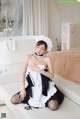 A woman in a maid outfit sitting on a bed.