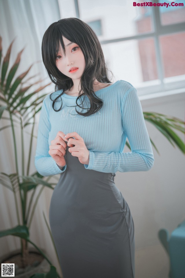 A woman in a blue top and gray skirt posing for a picture.