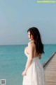 A woman in a white dress standing on a pier by the ocean.