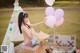 A naked woman sitting in front of a teepee holding a bunch of balloons.