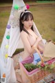 A naked woman sitting in front of a teepee with a basket of flowers.