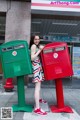 A woman standing next to a red and green mailbox.