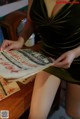 A woman in a green dress sitting at a table reading a newspaper.