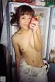 A naked woman holding a can of soda in front of a refrigerator.