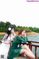 Two women sitting on a wooden bridge by the water.