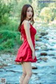 A woman in a red dress standing by a river.