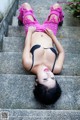 A woman in a pink top and black bikini laying on some steps.